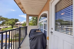 A balcony with a covered grill, a door with a window, and a view of a residential area. - NEW! Beachfront Condo! 2 MasterSuites! Gulf Views! (Long Beach)