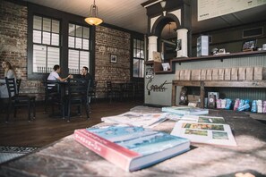 Een café met bakstenen muren, grote ramen en een rustieke houten tafel met boeken en koffiezakken.