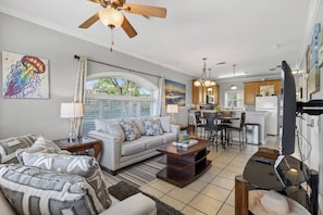 A living room with a sofa, coffee table, and a dining area with chairs and a table. - NEW! Beachfront Condo! 2 MasterSuites! Gulf Views! (Long Beach)