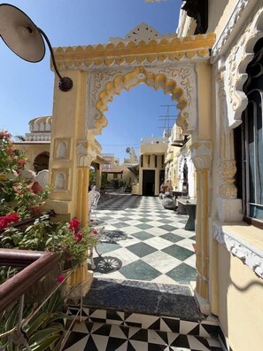 An outdoor corridor with a checkered floor, ornate arches, and potted plants. - Premium Heritage House (hiran magri udaipur)