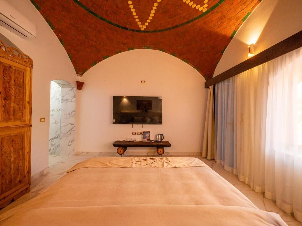 A bedroom with a bed, a television on the wall, a wooden cabinet, and a marble wall.