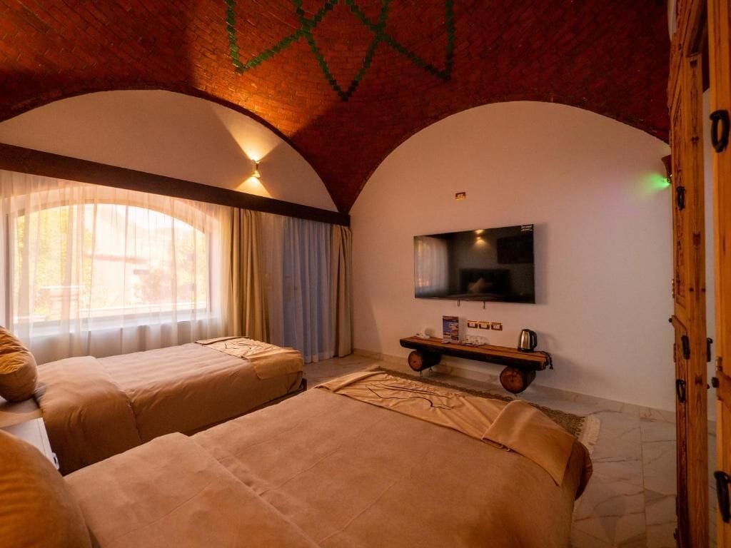 Une chambre d’hôtel avec deux lits, une télévision, une petite table avec un plateau, et une armoire en bois.