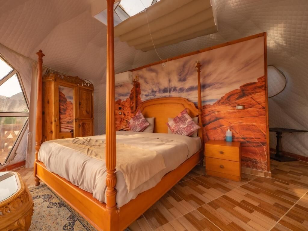 Ein Bett mit Baldachin, ein Holzkopfteil, ein Nachttisch und ein an der Wand befestigtes Fernsehgerät.