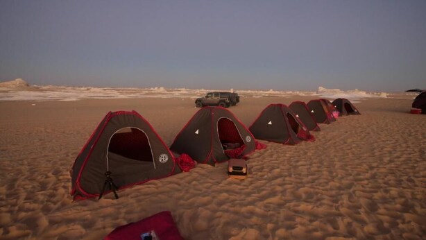A row of tents on a sandy beach with a vehicle in the background. - B&W Sahara Sky Hotel (Al Bawiti)