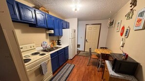 A compact kitchen with blue cabinets, a stove, a refrigerator, and a microwave. - Slew Shark Suite Number 4 (Crosby)