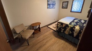 A small room with a bed, a chair, a small table, and two framed pictures on the wall. - Slew Shark Suite Number 4 (Crosby)