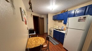 A compact kitchen with a dining table, chairs, a refrigerator, and blue cabinets. - Slew Shark Suite Number 4 (Crosby)
