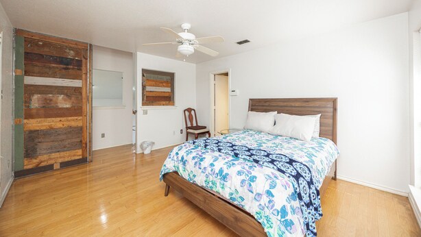 A bedroom with a wooden floor, a bed with a floral bedspread, a ceiling fan, and a wooden headboard. - Wooded Retreat Minutes from DFW Airport (Flower Mound)
