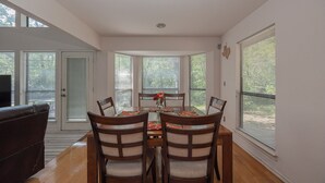 A dining area with a table set for four, surrounded by chairs, in a room with large windows and a door leading outside. - Wooded Retreat Minutes from DFW Airport (Flower Mound)