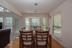 A dining area with a table set for four, surrounded by chairs, in a room with large windows and a door leading outside. - Wooded Retreat Minutes from DFW Airport (Flower Mound)