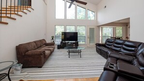 A spacious living room with a brown sofa, a black leather sofa, a glass coffee table, and a ceiling fan. - Wooded Retreat Minutes from DFW Airport (Flower Mound)