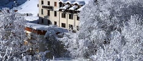 Un bâtiment recouvert de neige, doté de nombreuses fenêtres et de balcons, et entouré d’arbres également couverts de neige.