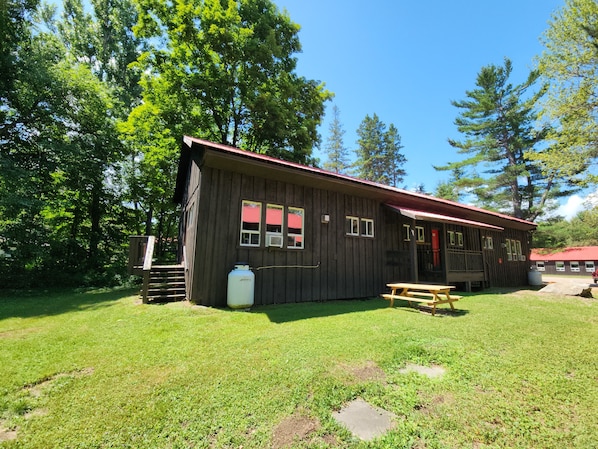 A rustic cabin with a red roof, a picnic table, and a large water tank.