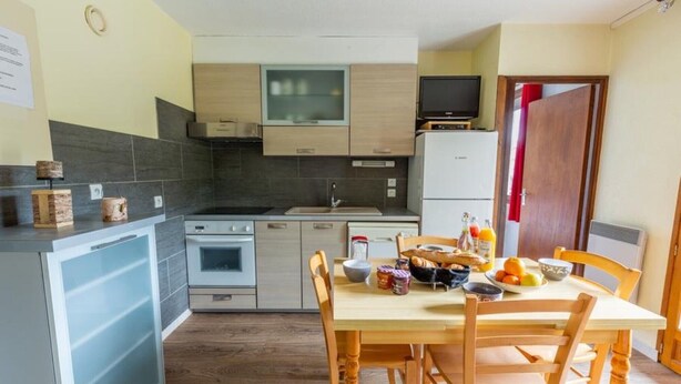 A compact kitchen with a dining area, including a refrigerator, oven, and a television. - Les Balcons de St So Apartment 1 – Mountain View, 2 Bedrooms, Near Slopes (Saint-Sorlin-d'Arves)