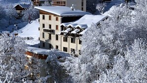 A snow-covered building with multiple windows and balconies, surrounded by trees also covered in snow. - Les Balcons de St So Apartment 1 – Mountain View, 2 Bedrooms, Near Slopes (Saint-Sorlin-d'Arves)