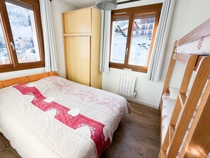 Ett sovrum med en säng, en trägarderob, två fönster med gardiner, ett element och utsikt över ett snötäckt landskap.