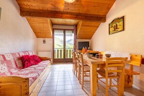 A cozy room with a wooden ceiling, a sofa with a red throw, a dining table with chairs, and a view of the outdoors through a door. - Les Balcons de St So Apartment A – 6/7 Guests, Ski-in/Ski-out, Mountain View, Parking (Saint-Sorlin-d'Arves)