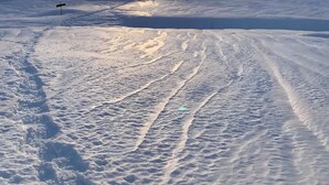 Paesaggio montuoso innevato con cielo sereno e sole visibile.