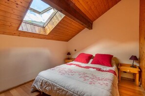 Una camera da letto con soffitto spiovente, una finestra a lucernario, un letto con cuscini rossi e lampade ai comodini.