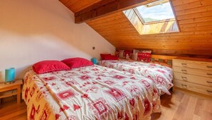 Una camera da letto con due letti, un lucernario, travi a vista in legno e un comò.