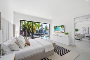 A modern bedroom with a large bed, a view of a pool and palm trees, and a painting of a beach scene. - Luxury House Waterfront Intracoastal Access (Fort Lauderdale)