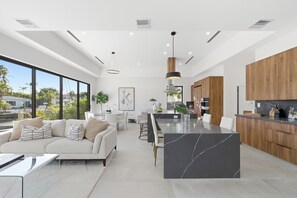 A modern kitchen with a central island, wooden cabinets, and a dining area with a white sofa and table. - Luxury House Waterfront Intracoastal Access (Fort Lauderdale)