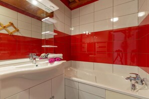 Ein Badezimmer mit weißem Waschbecken, einem Spiegel, einer Badewanne und roten Fliesenwänden.