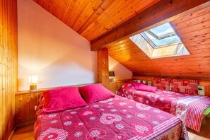 A cozy room with a sloped ceiling and a skylight, featuring two beds with matching red bedding and a small bedside table with a lamp. - Les Balcons de St So Apartment B – 3 Bedrooms, Ski-In/Ski-Out, Sleeps 8 (Saint-Sorlin-d'Arves)