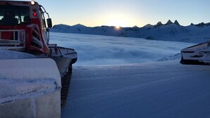 Paesaggio innevato con un veicolo rosso e un edificio parzialmente visibile.