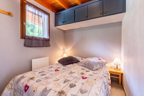 A bedroom with a bed, two bedside lamps, a window with curtains, and a ceiling with cabinets. - Les Balcons de St So Apartment C – 8 Guests, Ski-In/Ski-Out, Mountain View, 3 Bedrooms (Saint-Sorlin-d'Arves)