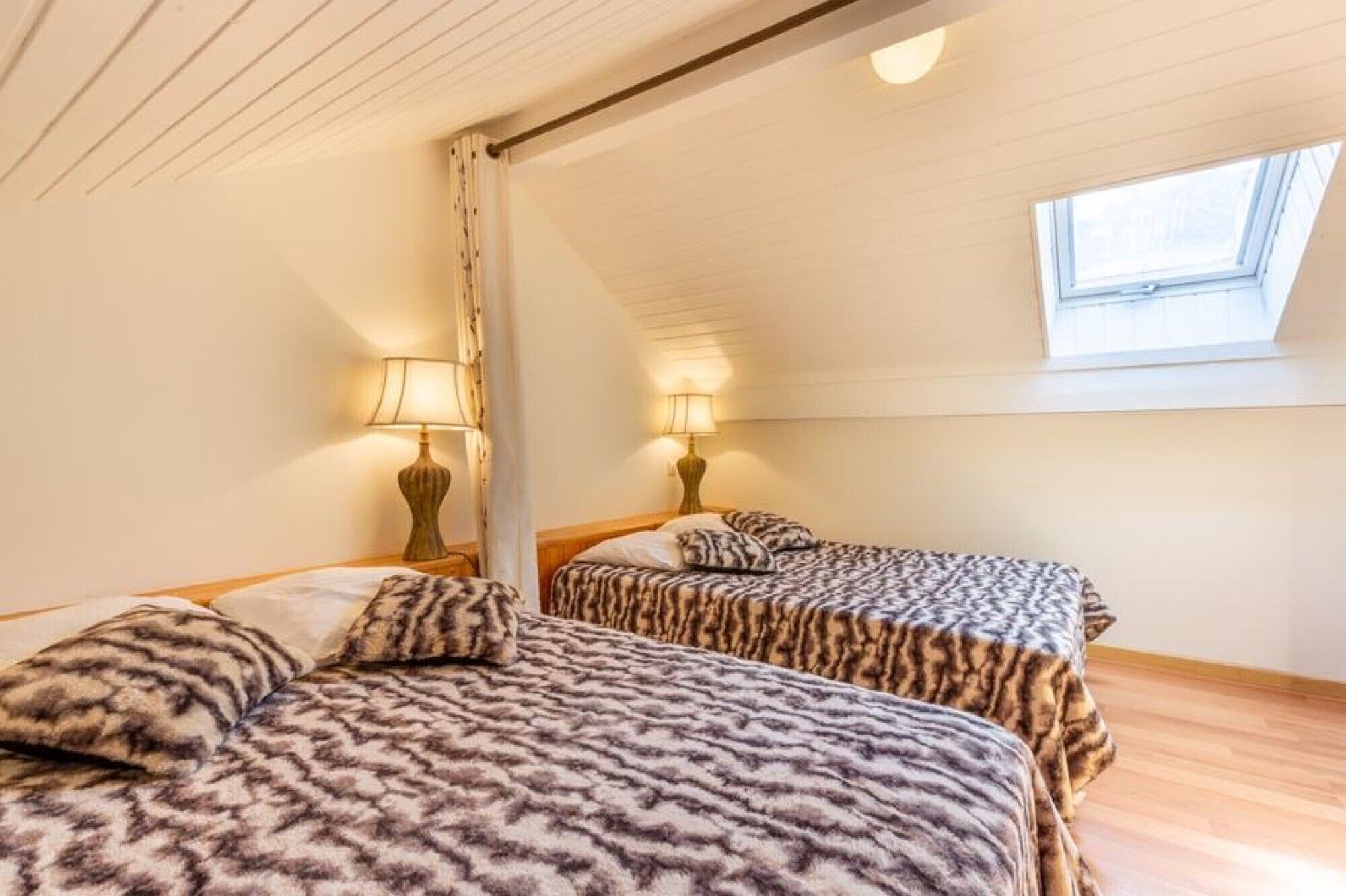 Una habitación con dos camas, cada una con una colcha estampada, una ventana y un tragaluz.