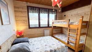A wooden cabin room with bunk beds, a window with curtains, a radiator, and a framed picture on the wall. - Les Balcons de St So Apartment D – Spacious, Sleeps 12, Near Slopes & Shops (Saint-Sorlin-d'Arves)