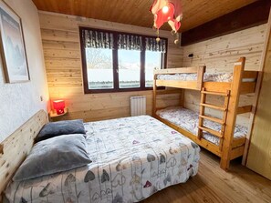 A wooden cabin room with bunk beds, a window with curtains, a radiator, and a framed picture on the wall. - Les Balcons de St So Apartment D – Spacious, Sleeps 12, Near Slopes & Shops (Saint-Sorlin-d'Arves)