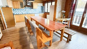 A wooden dining table with benches in a kitchen area with wooden cabinets and a checkered backsplash. - Les Balcons de St So Apartment D – Spacious, Sleeps 12, Near Slopes & Shops (Saint-Sorlin-d'Arves)