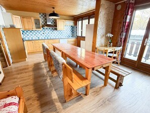 A wooden dining table with benches in a kitchen area with wooden cabinets and a checkered backsplash. - Les Balcons de St So Apartment D – Spacious, Sleeps 12, Near Slopes & Shops (Saint-Sorlin-d'Arves)
