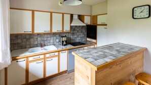 A compact kitchen with a central island, a built-in stove, and a coffee maker. - Les Balcons de St So Apartment 6 – 12 Guests, South-Facing Balcony, Near Slopes (Saint-Sorlin-d'Arves)