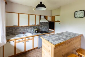 A compact kitchen with a central island, a built-in stove, and a coffee maker. - Les Balcons de St So Apartment 6 – 12 Guests, South-Facing Balcony, Near Slopes (Saint-Sorlin-d'Arves)