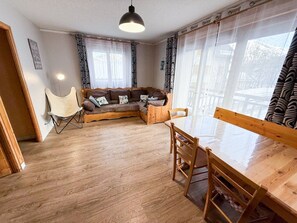 A cozy living area with a wooden sofa, a dining table, and chairs. - Les Balcons de St So Apartment 6 – 12 Guests, South-Facing Balcony, Near Slopes (Saint-Sorlin-d'Arves)