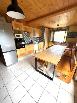 Eine moderne Küche mit Holzschränken, einem großen Esstisch und einem eingebauten Backofen.