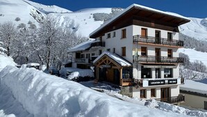 Un hotel a più piani con cartello che indica una pista da sci, circondato da alberi innevati e con montagne sullo sfondo.