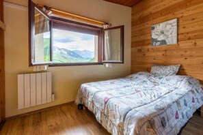 Ein Schlafzimmer mit Bett, einem Fenster mit Vorhängen, einem Heizkörper und einer Holzwand mit einem Gemälde.