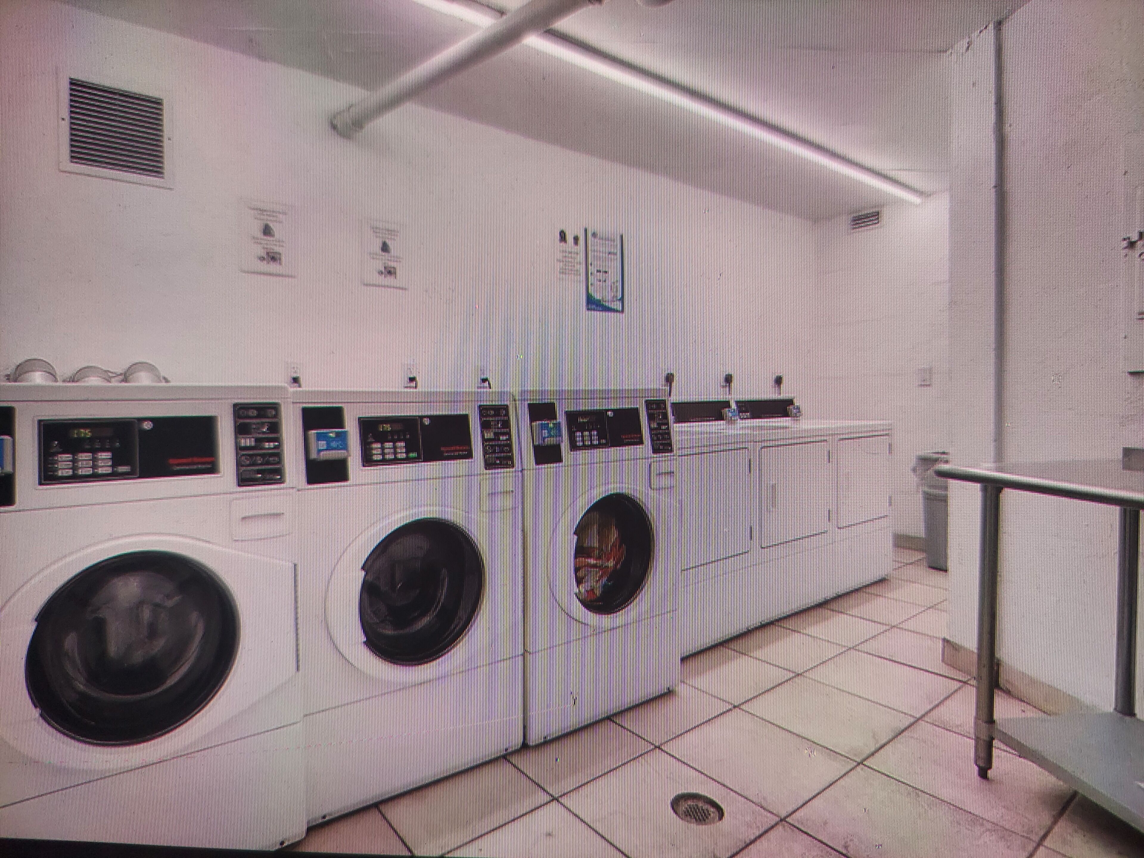 A laundry facility with multiple washing machines and dryers, a ventilation system, and a metal railing.