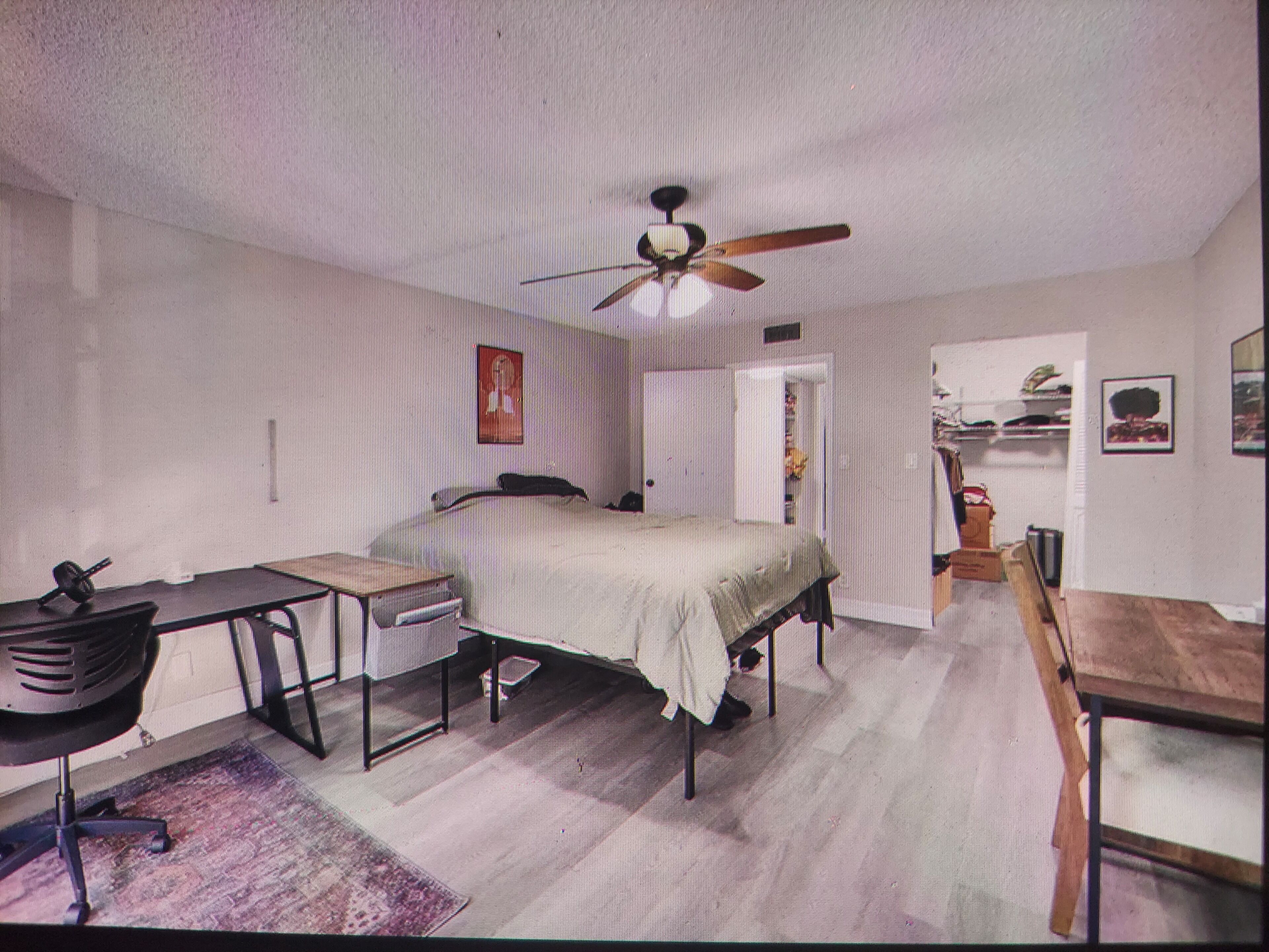 A bedroom with a bed, a desk, a chair, a ceiling fan, and a wardrobe.