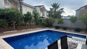 A rectangular swimming pool with a tiled edge, surrounded by a low wall and a variety of plants.