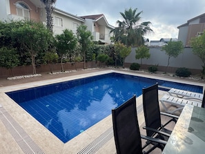 A rectangular swimming pool with a tiled edge, surrounded by a low wall and a variety of plants.