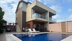 A modern two-story house with a swimming pool, outdoor furniture, and a covered patio area.