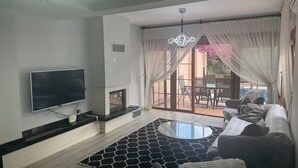 A living room with a flat-screen TV, a fireplace, a round glass coffee table, and a sofa.
