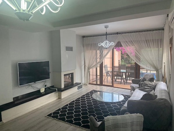 A living room with a flat-screen TV, a fireplace, a round glass coffee table, and a sofa.