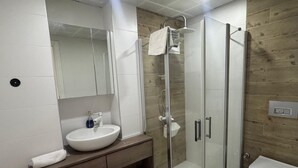 A modern bathroom with a glass-enclosed shower, a white sink, and a toilet.
