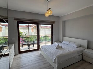 A bedroom with a bed, bedside tables, a wardrobe, a balcony with chairs, and a hanging light fixture. - Deluxe Villa with Private Pool (Antalya)